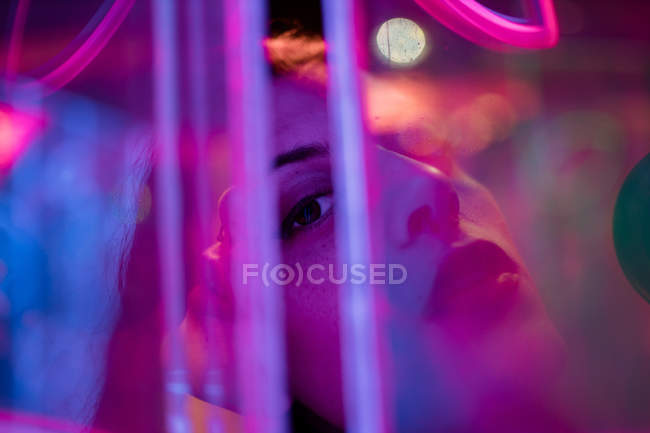 Close-up of woman looking in camera among colorful neon lights at city street — Stock Photo