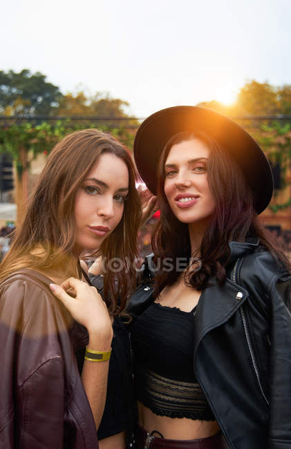 Charming long haired stylish girl friends confidently looking at camera in bright day at festival — Stock Photo