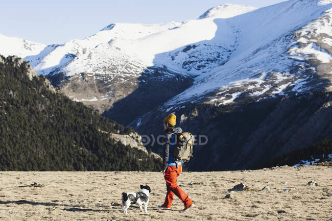 Турист з рюкзаком і собакою, що йде в долині проти засніженого мо — стокове фото