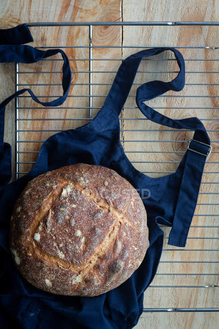 Top view of delicious brown round loaf of sourdough bread on black apron on oven lattice. — Stock Photo