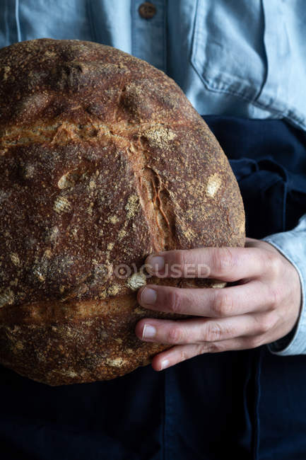Hand of anonymous woman holding loaf of homemade sourdough bread. — Stock Photo