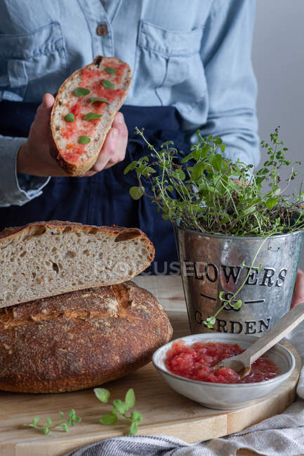 Unrecognizable female holding slice of sourdough bread with salsa over wooden table decorated with green plant — Stock Photo
