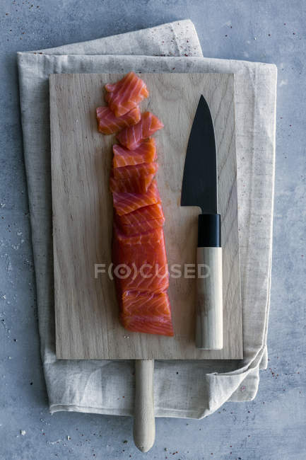 Dall'alto appetitoso salmone fresco a fette su tavola con asse di legno e coltello su asciugamano di lino — Foto stock