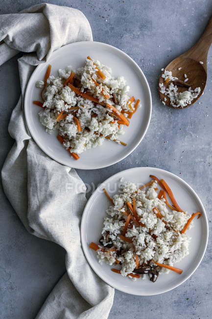 Сверху вкусный белый рис с овощами в тарелках и деревянной ложкой на столе — стоковое фото