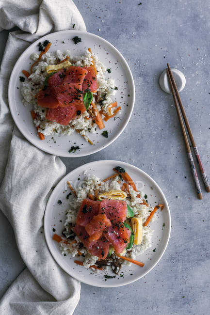 Вид зверху смачний апетитний нарізаний лосось на білому рисі з овочами в тарілках і паличками на столі — стокове фото