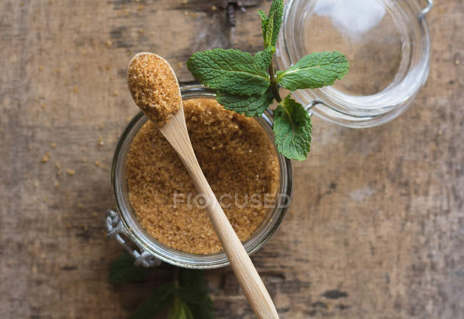 Sucre brun frais dans un bocal et feuilles de menthe poivrée placées sur une table en bois — Photo de stock