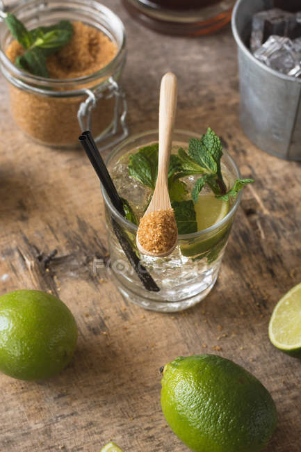 Frische Limetten und Pfefferminzblätter auf Serviette und Tisch in der Nähe von Rum und braunem Zucker zur Mojito-Zubereitung — Stockfoto