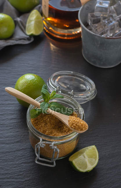 Von oben Glas kalten Mojito aus Rum und Limette mit Pfefferminze und braunem Zucker auf den feuchten Tisch in der Nähe von Eiswürfeln — Stockfoto
