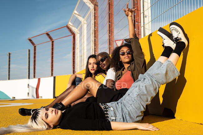 Konzentrierte junge multirassische Studentinnen in lässiger Kleidung schauen in die Kamera und ruhen sich auf dem Sportplatz aus — Stockfoto