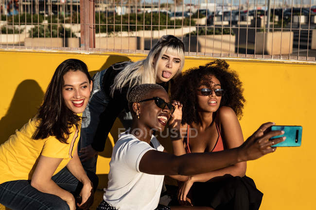 Cheerful young diverse female friends taking selfie on smartphone in street — Stock Photo