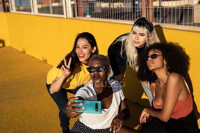 Cheerful young diverse female friends taking selfie on smartphone in street — Stock Photo
