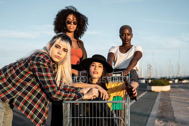 Grupo multirracial de jovens mulheres em pé em torno de carrinho de compras na estrada — Fotografia de Stock