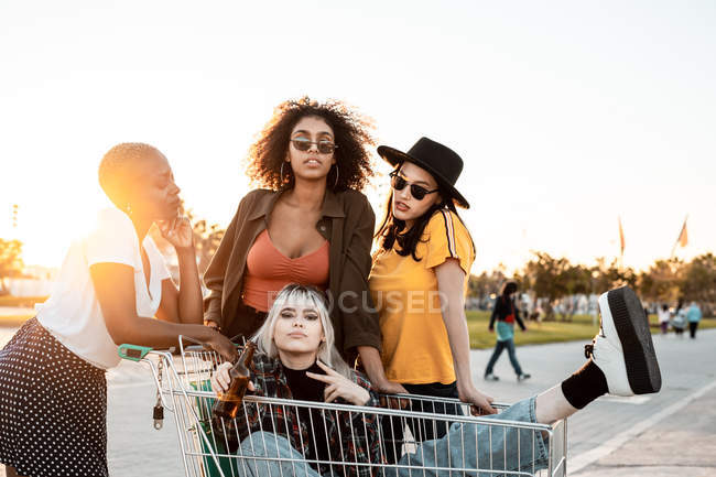 Grupo multirracial de mujeres jóvenes de pie alrededor del carrito de la compra en la carretera - foto de stock
