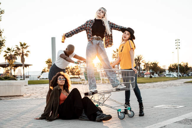 Multiracial group of young women standing around shopping cart on road — Stock Photo