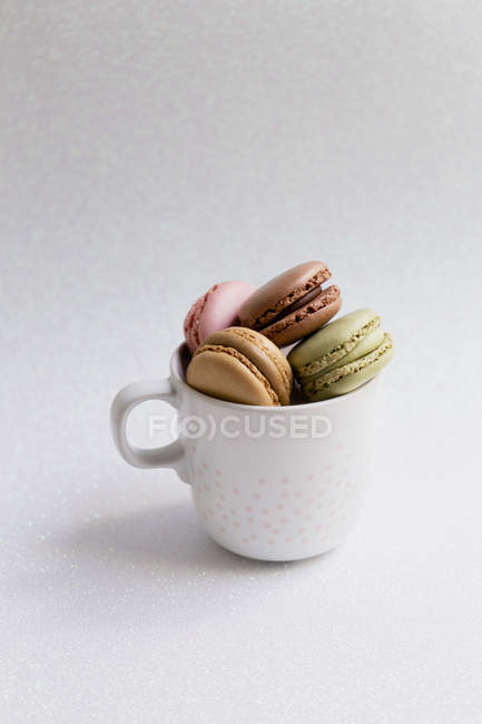 Vista ad alto angolo di tazza di teneri macaron colorati su sfondo bianco — Foto stock