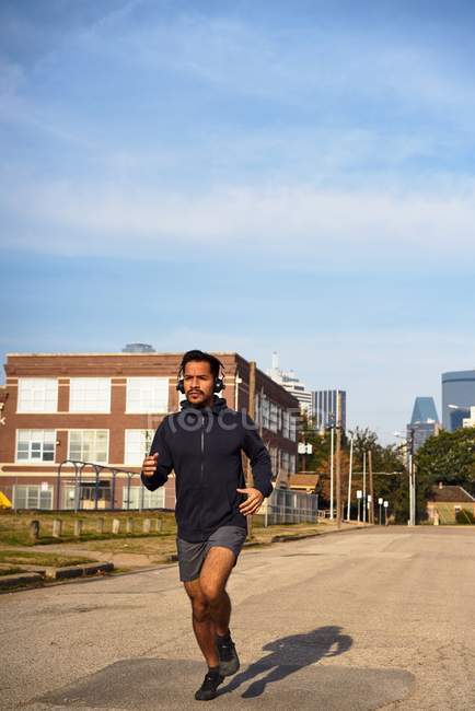 Athlète masculin hispanique concentré en vêtements de sport avec écouteurs courant le long de la route vide au centre-ville de Dallas, Texas — Photo de stock