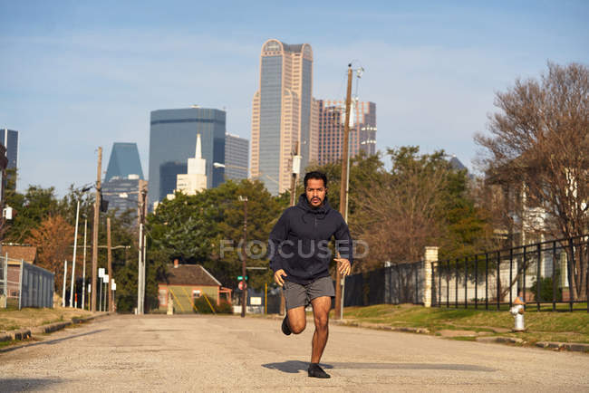 Athlète masculin hispanique concentré en vêtements de sport avec écouteurs courant le long de la route vide au centre-ville de Dallas, Texas — Photo de stock