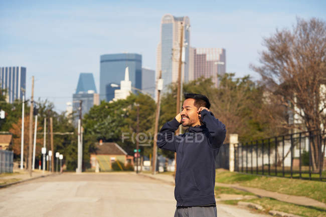 Satisfied Hispanic male athlete smiling while inserting earphones during morning jog at downtown — Stock Photo