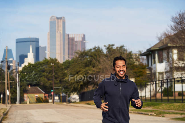 Happy Hispanic atleta masculino em sportswear com fones de ouvido correndo ao longo da estrada vazia no centro de Dallas — Fotografia de Stock