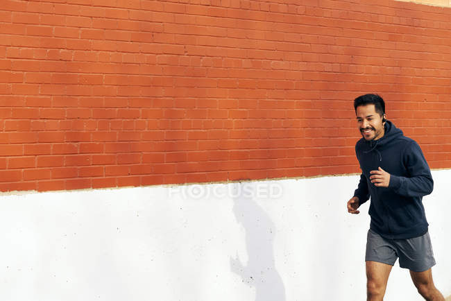 Vista laterale dell'uomo sportivo ispanico in forma che ascolta musica mentre fa jogging lungo la strada della città a Dallas — Foto stock