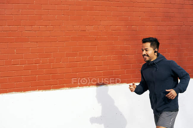 Side view of fit Hispanic sporty man listening music while jogging along city street in Dallas — Stock Photo