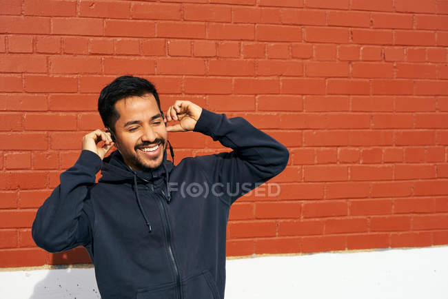 Hombre hispano con ropa casual sonriendo mientras disfruta de la música usando auriculares en la calle City en Dallas, Texas - foto de stock