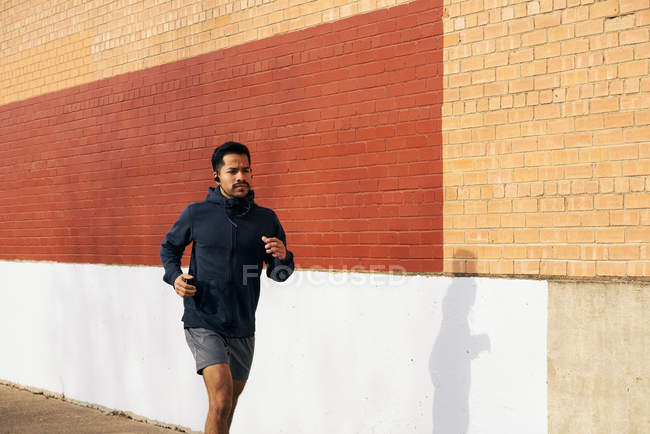 Vista laterale dell'uomo sportivo ispanico in abbigliamento attivo ascoltare musica mentre fa jogging lungo la strada della città a Dallas — Foto stock