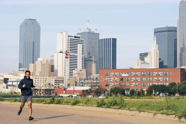 Überglücklicher hispanischer männlicher Läufer in aktiver Kleidung lachend und in die Kamera blickend in der mächtigen Innenstadt von Dallas, USA — Stockfoto