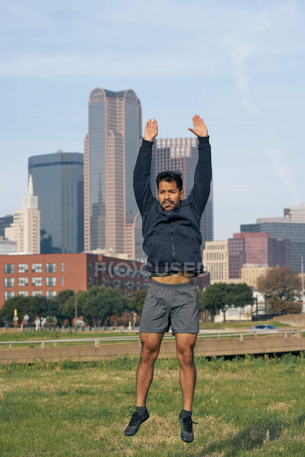 Atleta ispanico di sesso maschile in abbigliamento attivo che salta con le braccia allungate con il centro di Dallas, Texas, USA — Foto stock