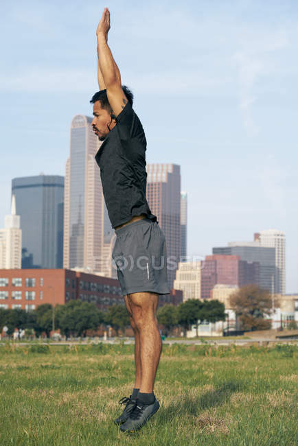 Atleta masculino hispânico em uso ativo pulando com braços estendidos com o centro da cidade de Dallas, Texas, EUA — Fotografia de Stock
