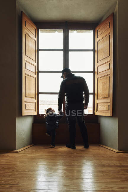 Padre e hijo tomados de la mano y mirándose el uno al otro cerca de wi - foto de stock