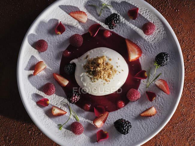 Walnuss gerieben auf cremigem Dessert mit Marmelade umgeben von Erdbeeren, Blaubeeren und Himbeeren auf weißem Teller — Stockfoto