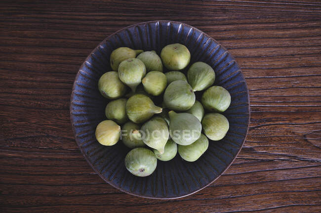 Сверху синяя декоративная чаша, полная мягких свежих инжиров на темном деревянном столе — стоковое фото