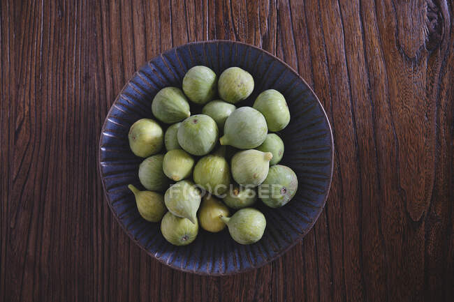 From above of blue ornamental bowl full of soft fresh figs on dark wooden table — Stock Photo