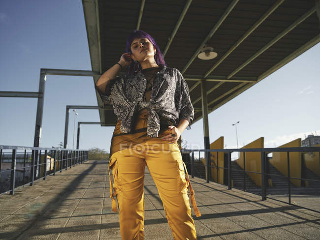 Desde abajo mujer con estilo de moda con peinado púrpura mirando en la cámara en la calle - foto de stock