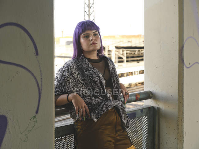 Модная стильная женщина с фиолетовой прической, отводящая взгляд и опирающаяся на перила — стоковое фото