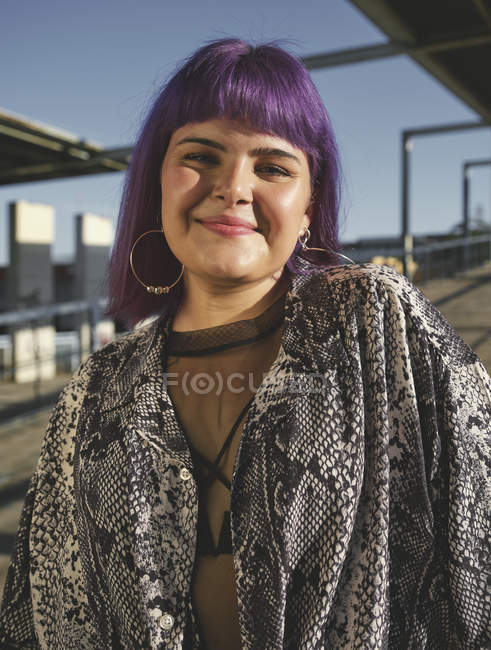 Портрет красивой улыбающейся молодой женщины с фиолетовой прической, стоящей на открытом воздухе — стоковое фото