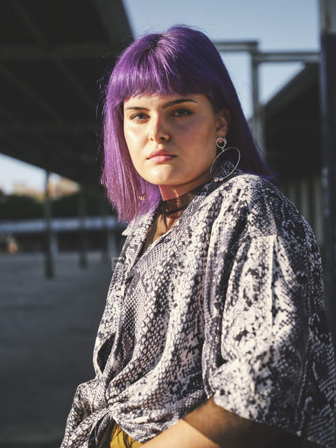 Стильна жінка з яскраво-фіолетовою зачіскою на міській станції, дивлячись в камеру — стокове фото