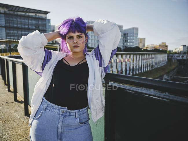 Модная женщина с фиолетовой прической, прикасающаяся к волосам и уверенно смотрящая в камеру — стоковое фото