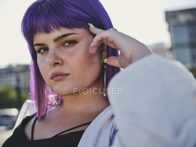 Крупним планом жінка з фіолетовою зачіскою торкається обличчя в центрі міста і впевнено дивиться в камеру — стокове фото