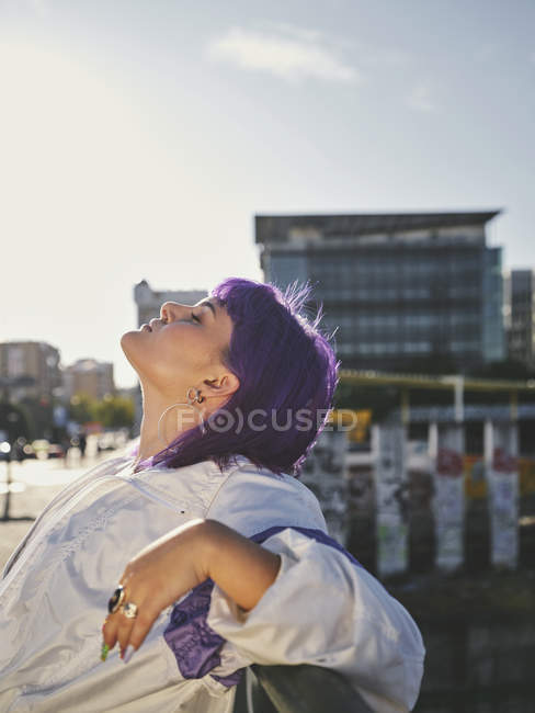 Стилістична жінка з фіолетовим волоссям спирається на металевий паркан у центрі міста. — стокове фото