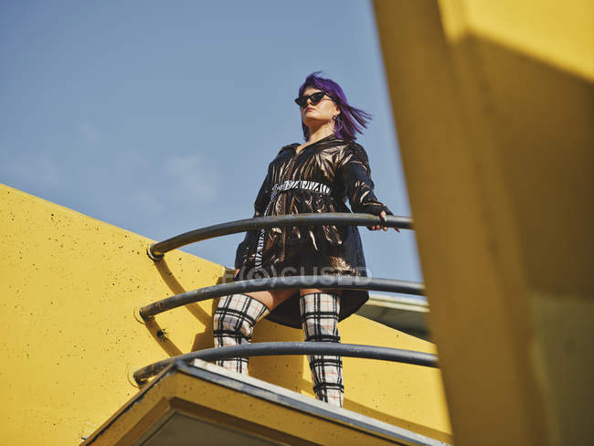 Снизу стильная женщина с фиолетовой прической, стоящая на смотровой площадке города — стоковое фото