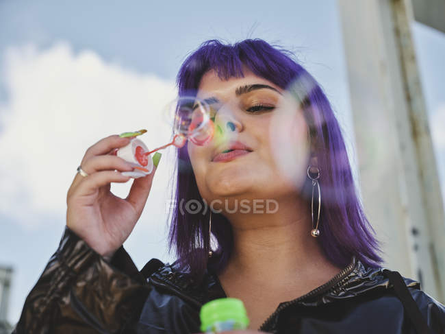 Retrato de mujer de moda con el pelo púrpura burbujas que soplan con la mano cuidada - foto de stock