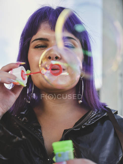 Portrait of fashionable woman with purple hair blowing bubbles with manicured hand — Stock Photo
