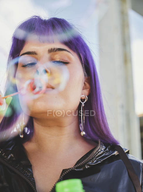 Retrato de mulher elegante com cabelo roxo soprando bolhas com mão cuidada — Fotografia de Stock