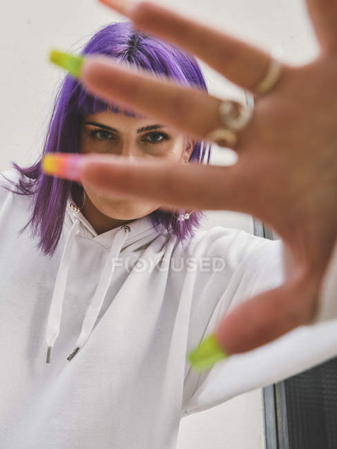 Mujer sonriente de moda con pelo morado gesticulando con la mano cuidada con anillos en los dedos, mirando en la cámara - foto de stock