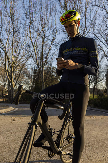 Man cyclist resting while using mobile phone on the bike lane in a park — Stock Photo