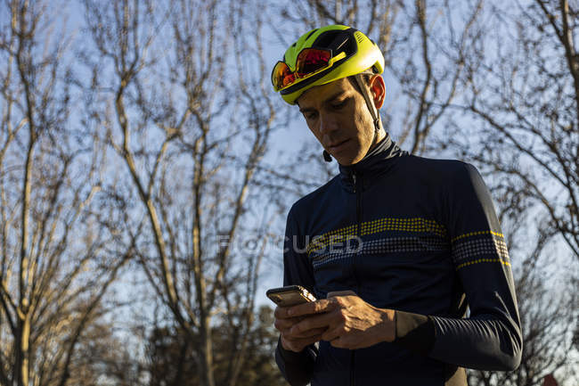 Велосипедист отдыхает, пользуясь мобильным телефоном на велосипедной дорожке в парке — стоковое фото