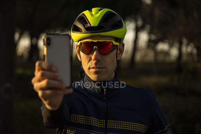 Man cyclist resting while using mobile phone to take a picture on the bike lane in a park — Stock Photo