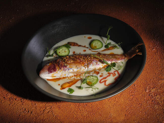 Вид зверху на смажену рибу в сковороді з соусом з огірком та травами та спеціями — стокове фото